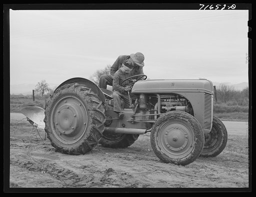 Tulare County, California. Farmer teaching his six-year old son to drive the tractor