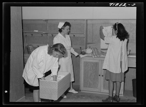 Girls who live at the NYA (National Youth Administration) resident center, located at the FSA (Farm Security Administration) farm workers' community at Eleven Mile Corner, learn baby care. The nurse, who divides her time between work at the hospital and instruction of NYA girls, is showing the girls