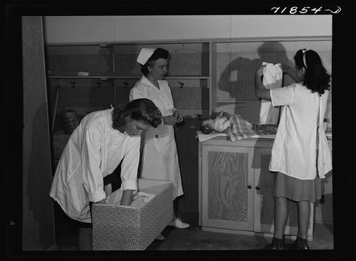 Eleven Mile Corner, Arizona. FSA (Farm Security Administration) farm workers' community. Girls, who live at the NYA (National Youth Administration) resident center learning baby care. The nurse, who divides her time between working at the hospital and instructing the NYA girls, is showing them how t