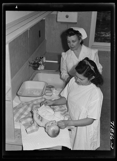 Eleven Mile Corner, Arizona. FSA (Farm Security Administration) farm workers' community. Girls who live at the NYA (National Youth Administration) resident center learning baby care. The nurse, who divides her time between working at the hospital and instructing the NYA girls, is showing them how to