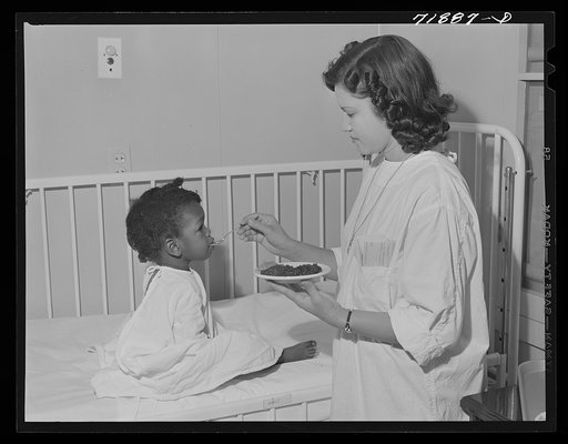 NYA (National Youth Association) girl feeds lunch to little girl who is a patient at the Cairns General Hospital located at the FSA (Farm Security Administration) farm workers' community at Eleven Mile Corner, Arizona