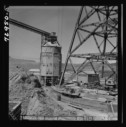 Untitled photo, possibly related to: Shasta Dam, Shasta County, California. Foot of head tower from which cable buckets operate at the dam. Structure on left is concrete mixing depot. The car, which runs on tracks, is filled with concrete and takes it to point where the cable buckets are filled