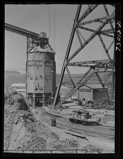 Shasta Dam, Shasta County, California. Foot of head tower from which cable buckets operate at the dam. Structure on left is concrete mixing depot. The car, which runs on tracks, is filled with concrete and takes it to point where the cable buckets are filled