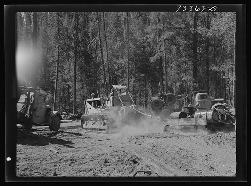 Untitled photo, possibly related to: Grant County, Oregon. Malheur National Forest. Diesel caterpillar tractor, log truck and trailer. The trailer folds when not in use for hauling logs