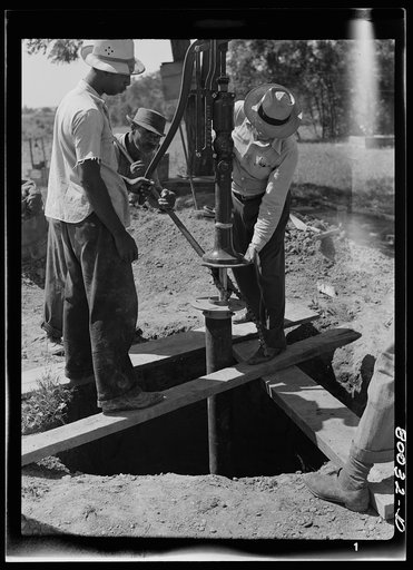 Pump is settled onto pump rod and drop pipe. Pipe wrench still keeps drop pipe from slipping into well. John Fredrick well project, St. Marys County, Maryland