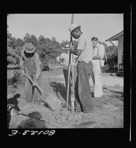 Tamping in earth around top of pump after fill of gravel has been poured around the casing. Ridge well project, Saint Mary's County, Maryland