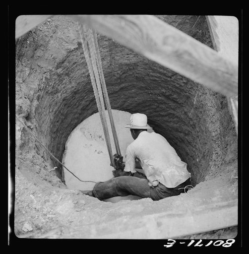 The cement well cap is lowered down the cleared well with a two purchase block and tackle. John Hardesty well project, Charles County, Maryland