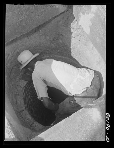 Well worker balances on siding of brick, removing them one at a time to the depth of ten feet, where the bricks will form a base for the cement cap. John Hardesty well project, Charles County, Maryland