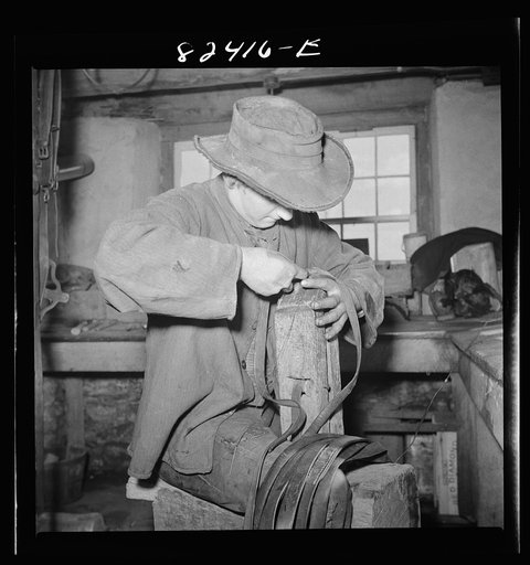 Honey Brook, Pennsylvania (vicinity). Amish farmhand mending harness on the Zook farm