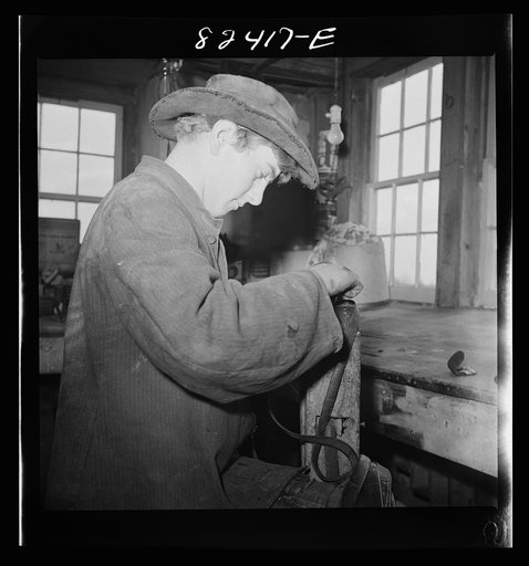 Honey Brook, Pennsylvania (vicinity). Amish farmhand mending harness on the Zook farm