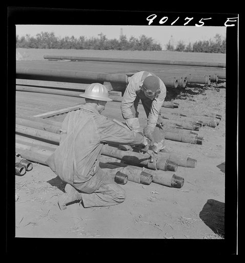 Knocking tool joints off a drill pipe, after welder has cut it. In Goodrich field of Continental oil field near Wichita, Kansas
