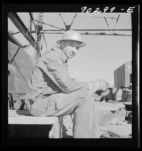 J.E. Schenermann, driller from Oklahoma, but worked in the Kansas oil fields about ten years; on pile of drill pipes near oil well in Goodrich field of Continental oil company. Valley Center oil field near Wichita, Kansas