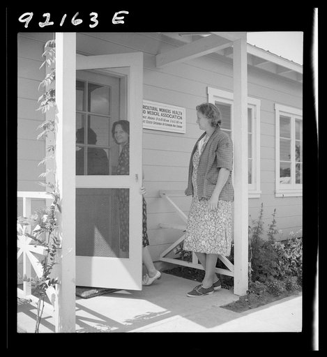 Untitled photo, possibly related to: Tulare County, Farmersville, California. Farm Security Administration (FSA) camp for migratory agricultural workers. Entering clinic of Agricultural Workers' Health and Medical Association (FSA) for nurse's help with sick baby. Older woman says, "I'm just a neigh