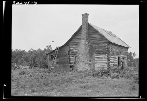 Untitled photo, possibly related to: Negro sharecropper house. Note chimney leanto with kitchen stove pipe stuffed through side of wall and cap off with joint of tobacco flue to keep smoke from blowing back into house. Note also flower garden protected by slender fence of lathes. Person County, Nort