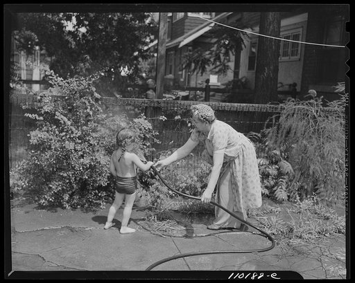 Detroit, Michigan. Elder woman helping little girl to spray grass with a hose