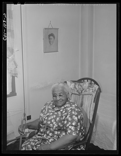 Portrait of Mrs. Ella Patterson, the oldest resident at the Ida B. Wells Housing Project, Chicago, Illinois. She is 102 years old. On the wall hangs a picture of her daughter