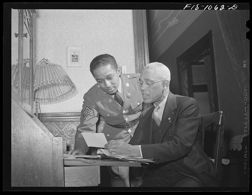 Baltimore, Maryland. Sargeant Franklin Williams, home on leave from Army duty, discussing insurance problems with his father