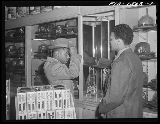 Chicago, Illinois. Mr. Claude Walker trying on a new hat in the Henry C. Taylor Store For Men, 47th Street near State. The salesman is Mr. William Strong, who is manager of the store