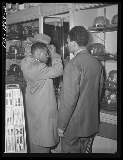 Chicago, Illinois. Mr. Claude Walker trying on a new hat in the Henry C. Taylor Store For Men, 47th Street near State. The salesman is Mr. William Strong, who is manager of the store