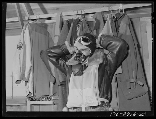 One of the "Flying Sergeants" dons his oxygen apparatus for high altitude flying. Immediately over his heavy flying suit is his "Mae West" life preserver, which is easily inflated. Lake Muroc, California