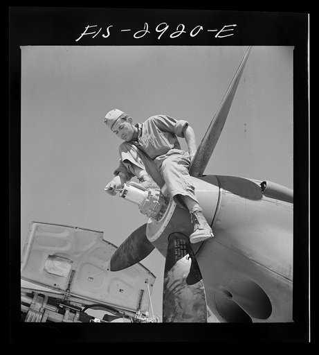 Repair man perched upon propeller hub of airplane. Lake Muroc, California