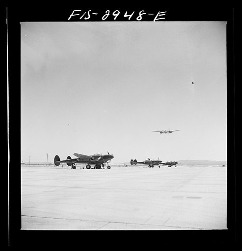 "Buzzing" the field. Member of interceptor squadron swoops low over parked airplanes to simulate a strafing attack on an airport. Lake Muroc, California