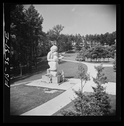 Greenbelt, Maryland. Federal housing project. View from roof of shopping center showing statue of a mother and child with a drinking fountain. Apartment houses are in the background