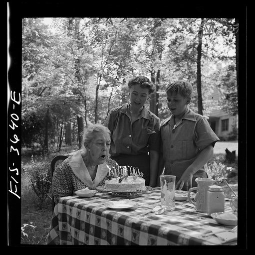 Greenbelt, Maryland. Grandma Taylor blows out the candles on her eighty-third birthday cake while her daughter, Mrs. McCarl, and grandson look on