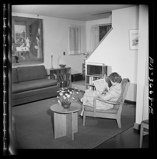 Greenbelt, Maryland. Mrs. Hoover reading a copy of the Greenbelt Cooperator in her living room. One the opposite wall is an American primitive painting