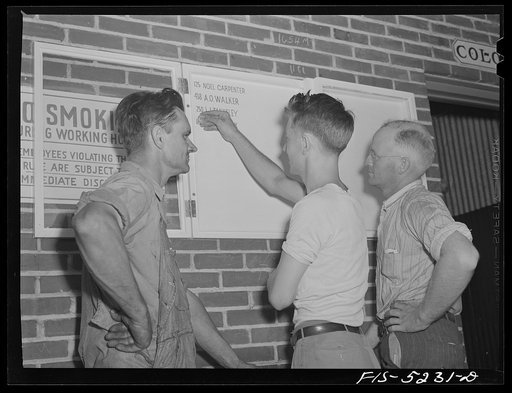 Decatur, Alabama. Ingalls Shipbuilding Company. Morris Black, timekeeper, going off to the army, pinning up his badge on the bulletin board reserved for men from the yard who have joined the armed forces. Two of his friends look on