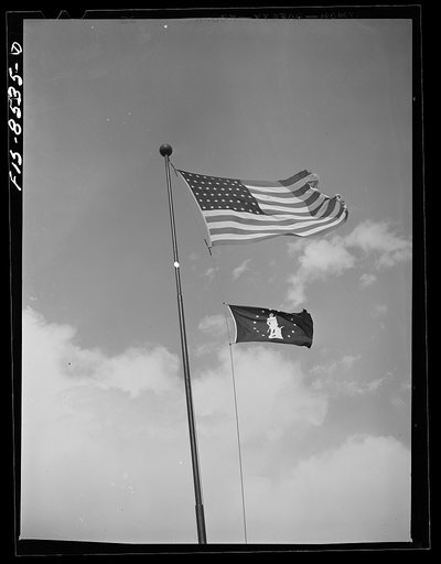Flag of Minutemen floats beneath the national flag. This minuteman flag signifies that over ninety percent of the workmen place ten percent of their wages in United States war bonds