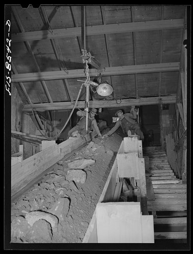 Anaconda smelter, Montana. Anaconda Copper Mining Company. Two workmen remove wood and particles of timber from the mine-run ore as it is conveyed from the unloading bin to the first or gyratory crusher