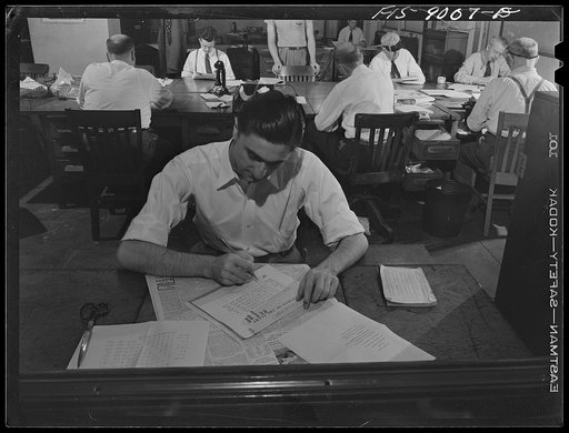 New York, New York. Sports department of the New York Times newspaper. In foreground, working out a table of baseball scores. In background is sports desk. Copy readers and editors wait for new copy