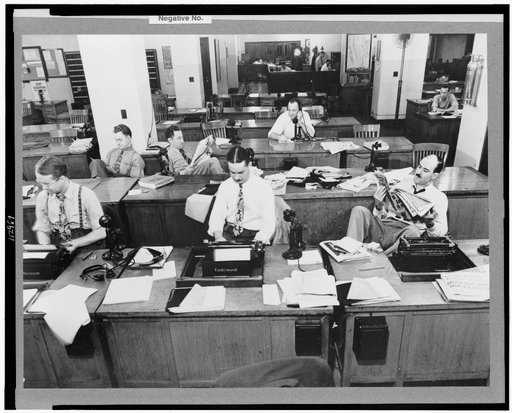 New York, New York. Newsroom of the New York Times newspaper. Reporters and rewrite men writing stories, and waiting to be sent out. Rewrite man in background gets the story on the phone from reporter outside