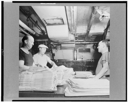 New York, New York. Mailroom of the New York Times newspaper. Papers, delivered from press room on a conveyor, are tied into packages according to orders from retailers