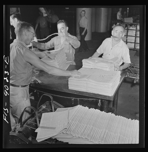 New York, New York. Mailroom of the New York Times newspaper. Papers, delivered from press room on a conveyor, are tied into packages according to orders from retailers