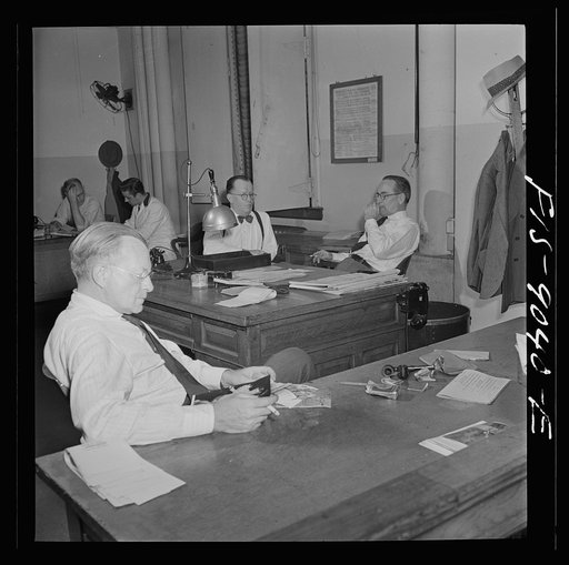 New York, New York. News room of the New York Times newspaper. The "bull pen" where managing editors and others sit at one side. In the foreground, assistant managing editor Rae. In background, managing editor James and night managing editor McCaw conferring