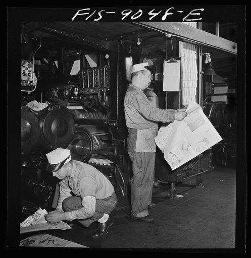 New York, New York. Pressroom of the New York Times newspaper. As presses are rollig and finished papers start coming off (see background), pressmen read the paper to catch defective press work. Pressman in foreground is filling ink fount