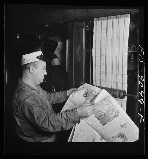 New York, New York. Pressroom of the New York Times newspaper. Pressman reading first edition as it comes off presses on conveyor, to detect defective press work