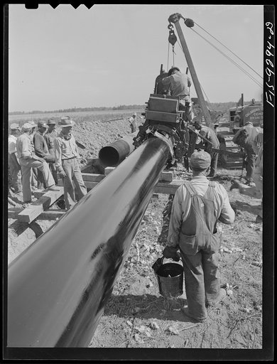 Little Rock, Arkansas to Missouri-Arkansas state line. War emergency pipeline from Longview, Texas to Norris City, Illinois. Priming pipe with hot asphalt paint. Crew follows machine and touches up by hand the space where pipe is welded together