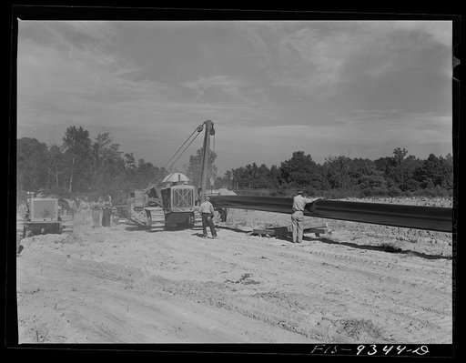 Little Rock, Arkansas to Missouri-Arkansas state line. War emergency pipeline from Longview, Texas to Norris City, Illinois. Doping gang wrapping primed pipe with felt. A workman moves ahead of wrapping machine wiping dust off pipe