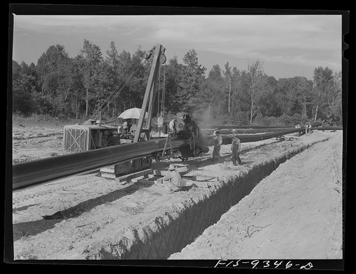 Untitled photo, possibly related to: Little Rock, Arkansas to Missouri-Arkansas state line. War emergency pipeline from Longview, Texas to Norris City, Illinois. Doping gang wrapping primed pipe with felt. A workman moves ahead of wrapping machine wiping dust off pipe