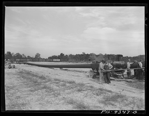 Untitled photo, possibly related to: Little Rock, Arkansas to Missouri-Arkansas state line. War emergency pipeline from Longview, Texas to Norris City, Illinois. Doping gang wrapping primed pipe with felt. A workman moves ahead of wrapping machine wiping dust off pipe
