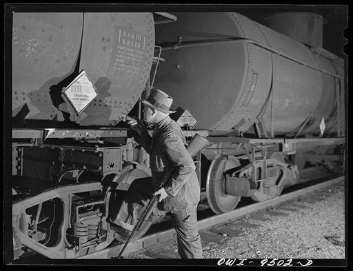 Tulsa, Oklahoma. Armed railroad guard inspecting an oil tank car in the yards