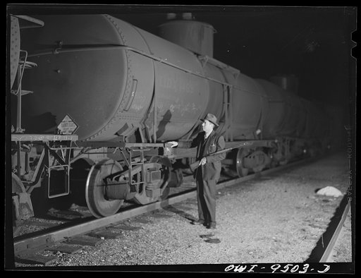 Tulsa, Oklahoma. Armed railroad guard inspecting an oil tank car in the yards