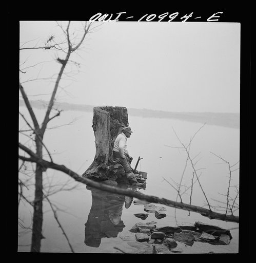 Untitled photo, possibly related to: Lancaster County, Pennsylvania. Fishing for salmon on the Susquehanna River at 6 p.m. This man is a state supervisor of highways. In his time off late in the afternoon he fishes with a bottle of hard cider beside him