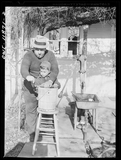 Untitled photo, possibly related to: Neffsville, Pennsylvania. Earle Landis freezing ice cream on the back porch on Thanksgiving day. When it gets hard, his son sits on the freezer to hold it down
