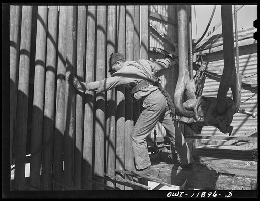 Andrews County, Texas. Derrick man moving pipe into position as it is brought up out of the hole for changing the bit
