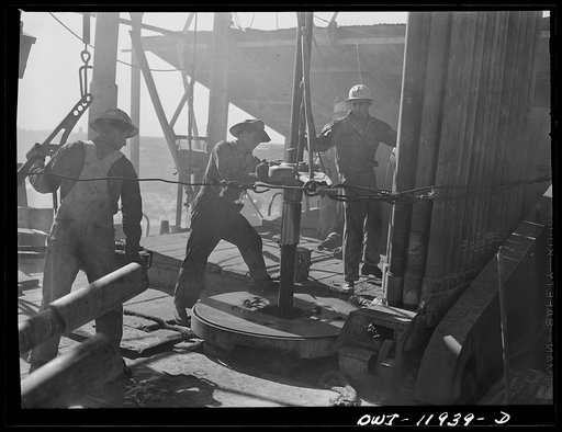 Andrews County, Texas. Unscrewing a piece of drill pipe by means of a rotary table. The pipe is being pulled out of the well to change the bit