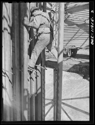 Andrews County, Texas. Derrick man putting pulled drill pipe in place. He is 120 feet above the ground